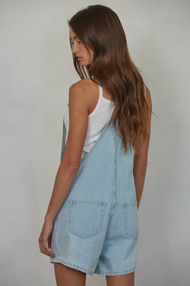 Woman wearing light blue denim overalls against a plain background