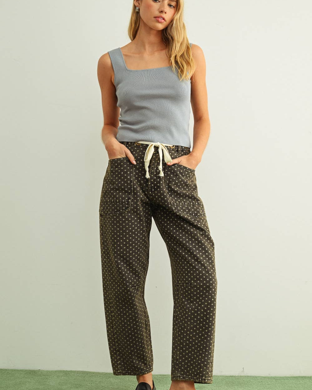 Woman wearing a light blue tank top and patterned pants on a plain background