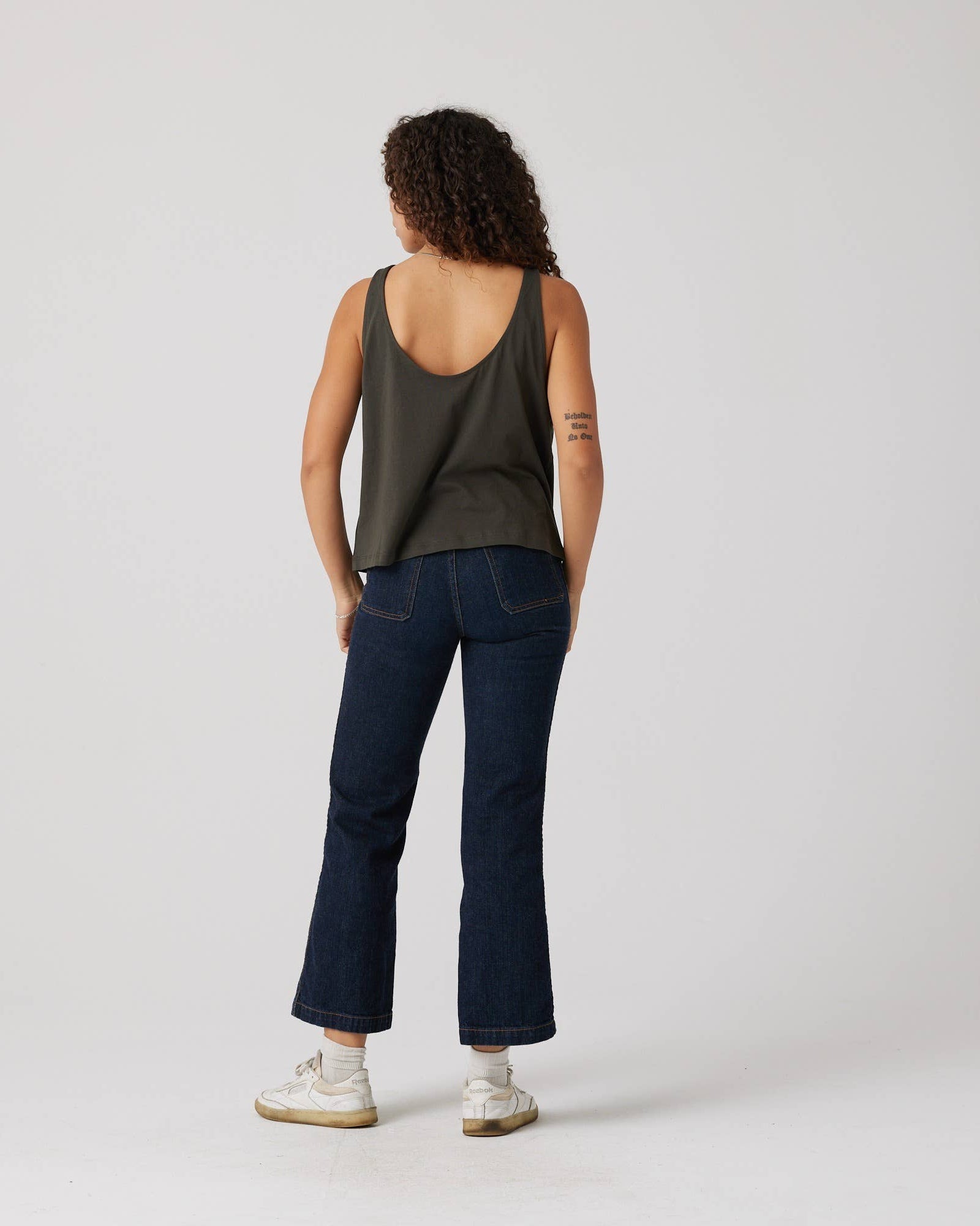 Person wearing a green tank top and dark blue jeans on a white background
