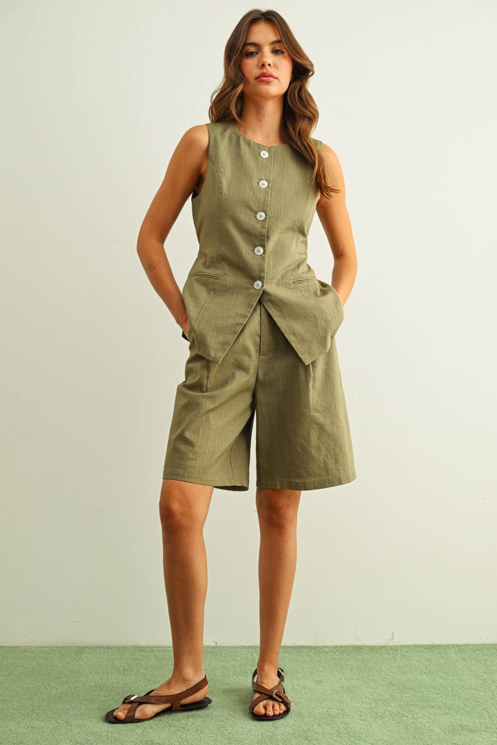 Woman wearing a green sleeveless jumpsuit with buttons on a light background