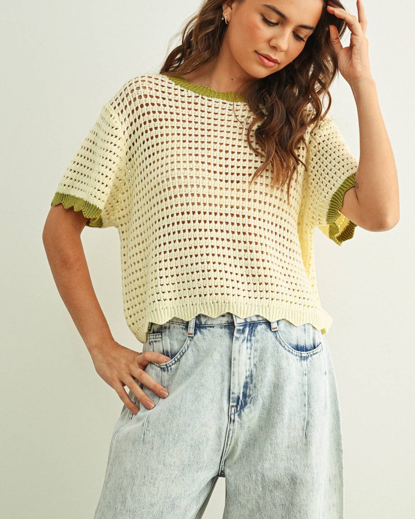 Woman wearing a yellow crochet top and light blue jeans against a plain background