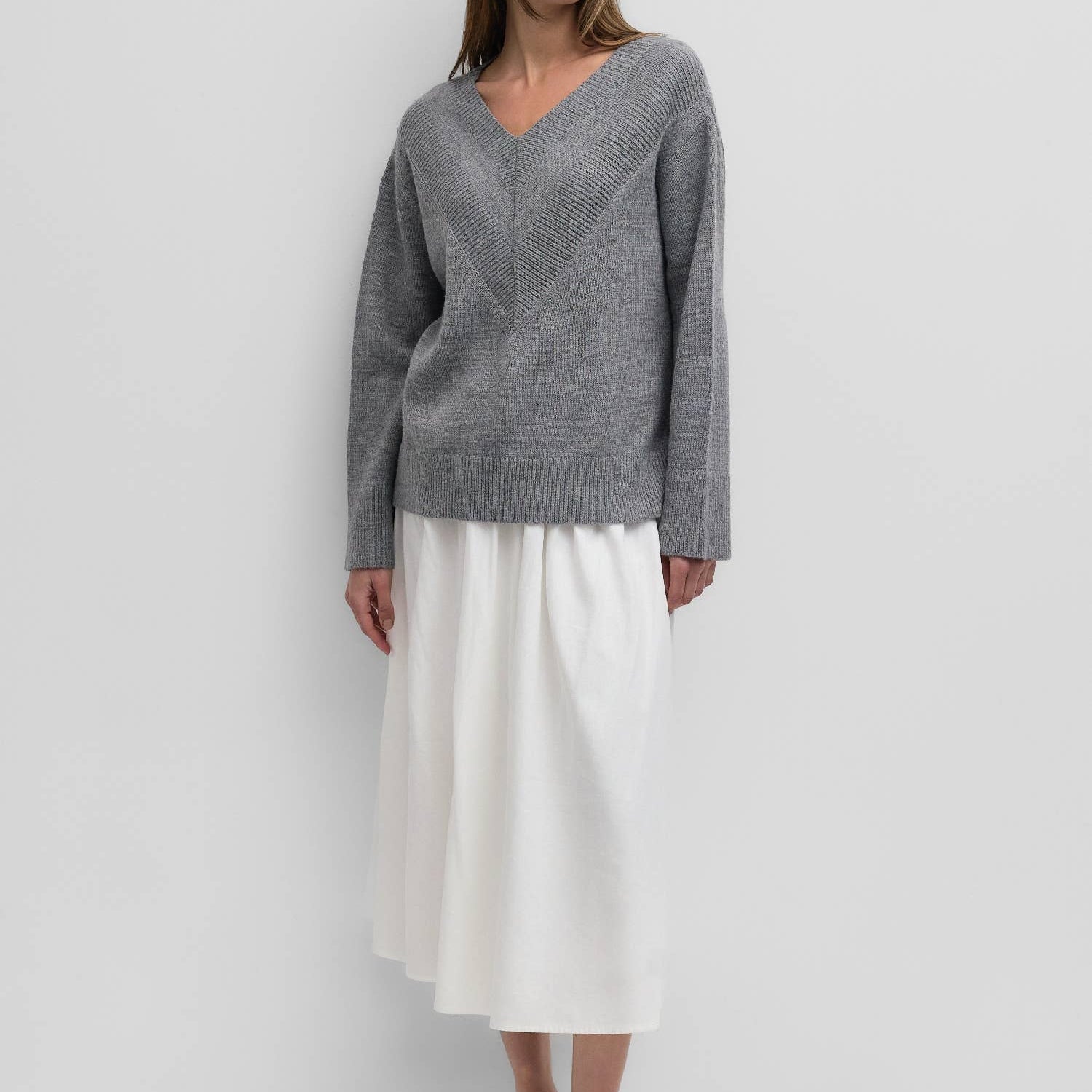 Woman wearing a gray sweater and white skirt against a white background