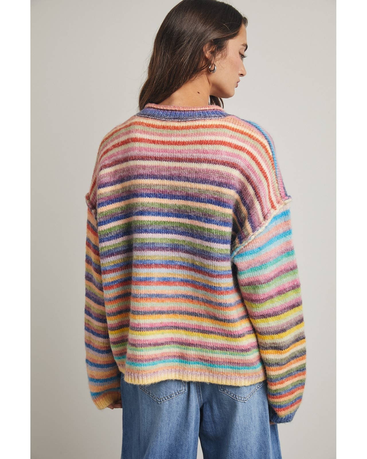 Person wearing a colorful striped sweater and blue jeans against a plain background