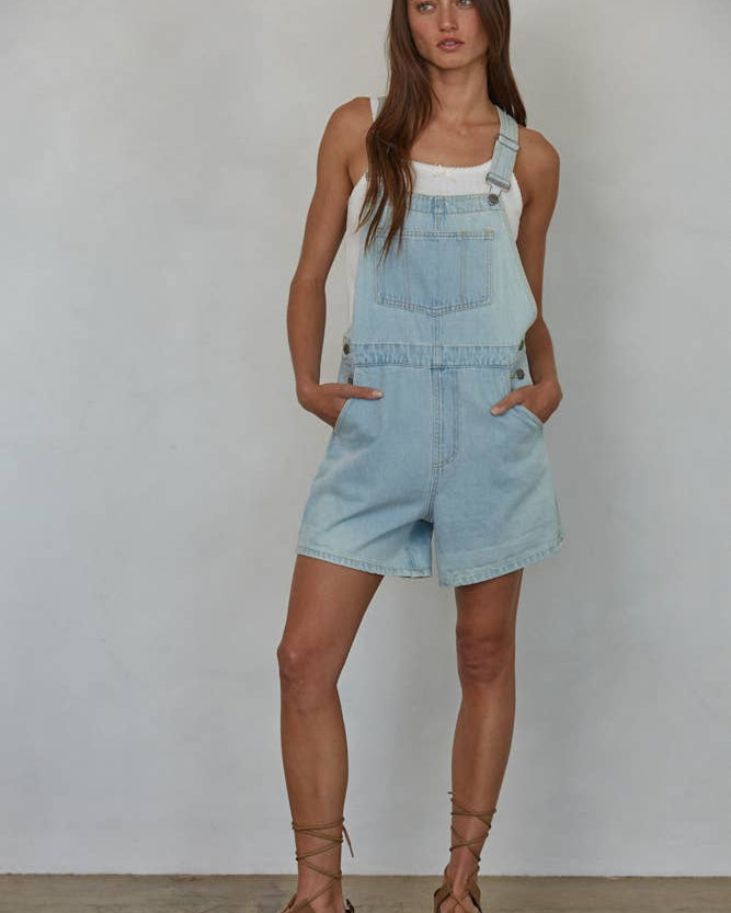 Woman wearing a light blue denim overall dress against a plain background
