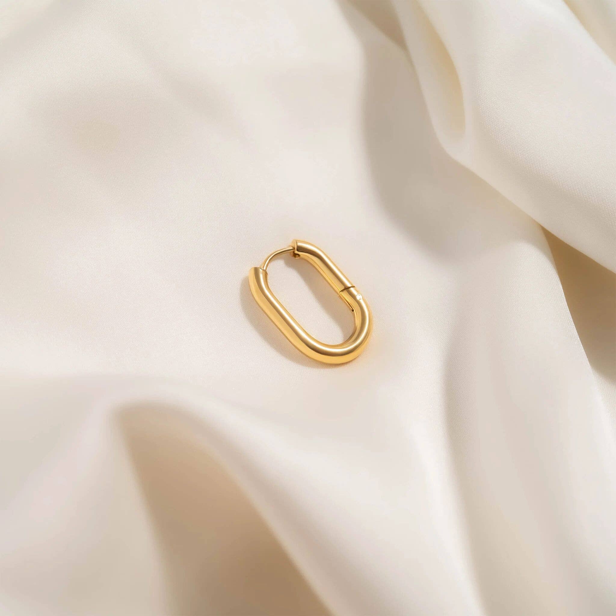 Gold hoop earring on a soft beige fabric background