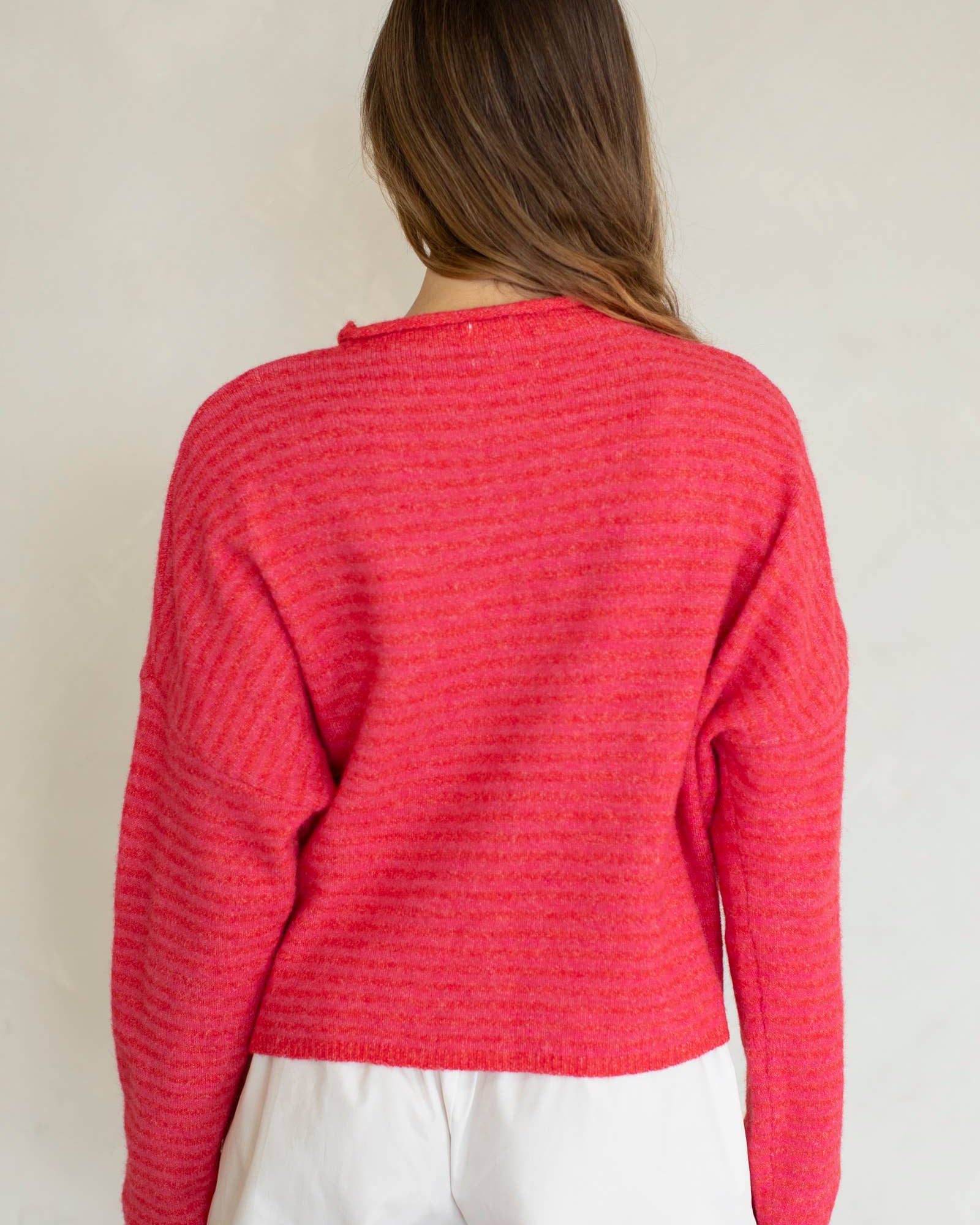 Person wearing a red textured sweater and white pants against a plain background