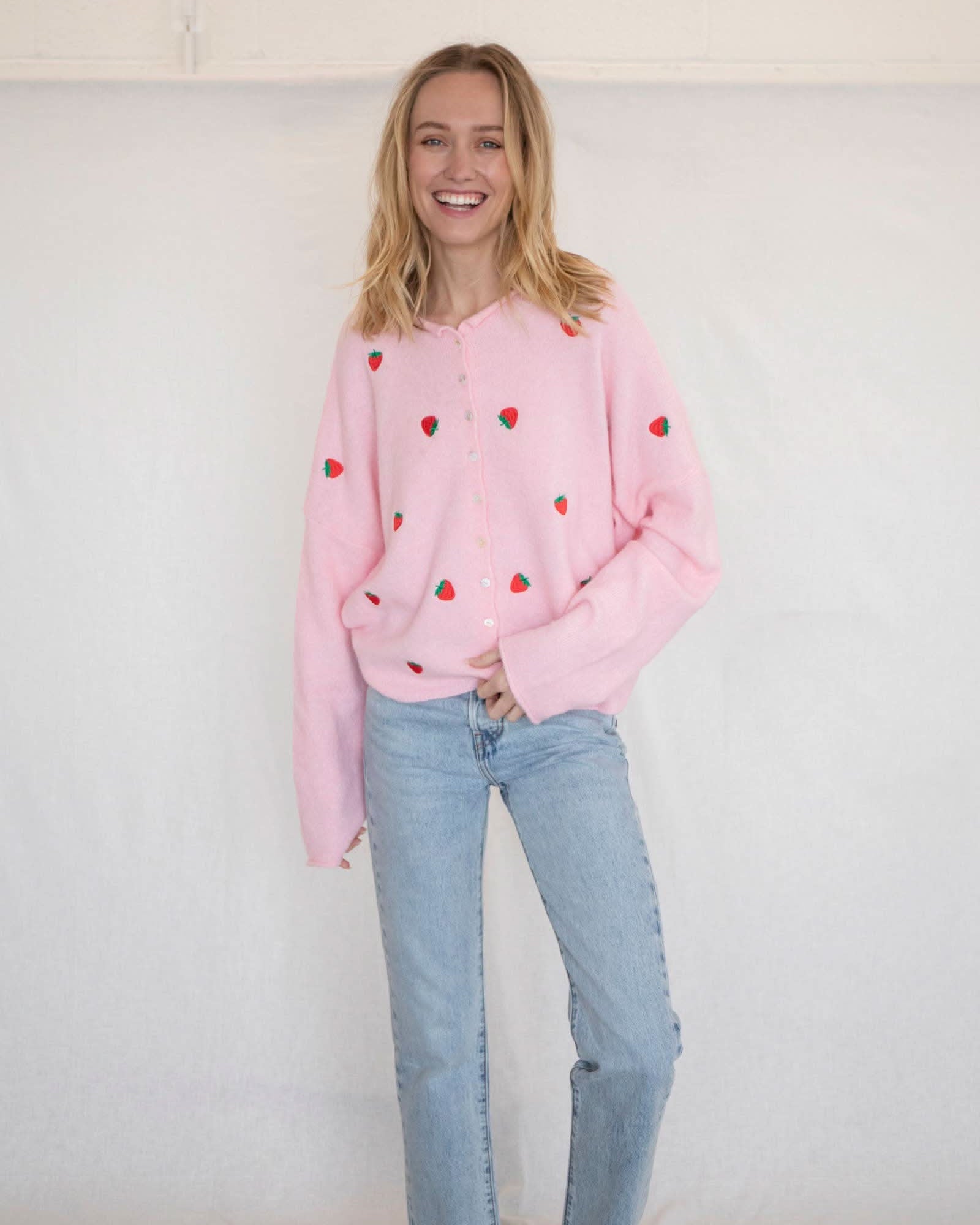 Woman wearing a pink button down cardigan with strawberries and blue jeans