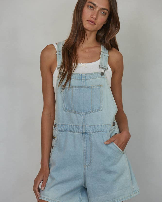 Woman wearing light blue denim overalls against a plain background