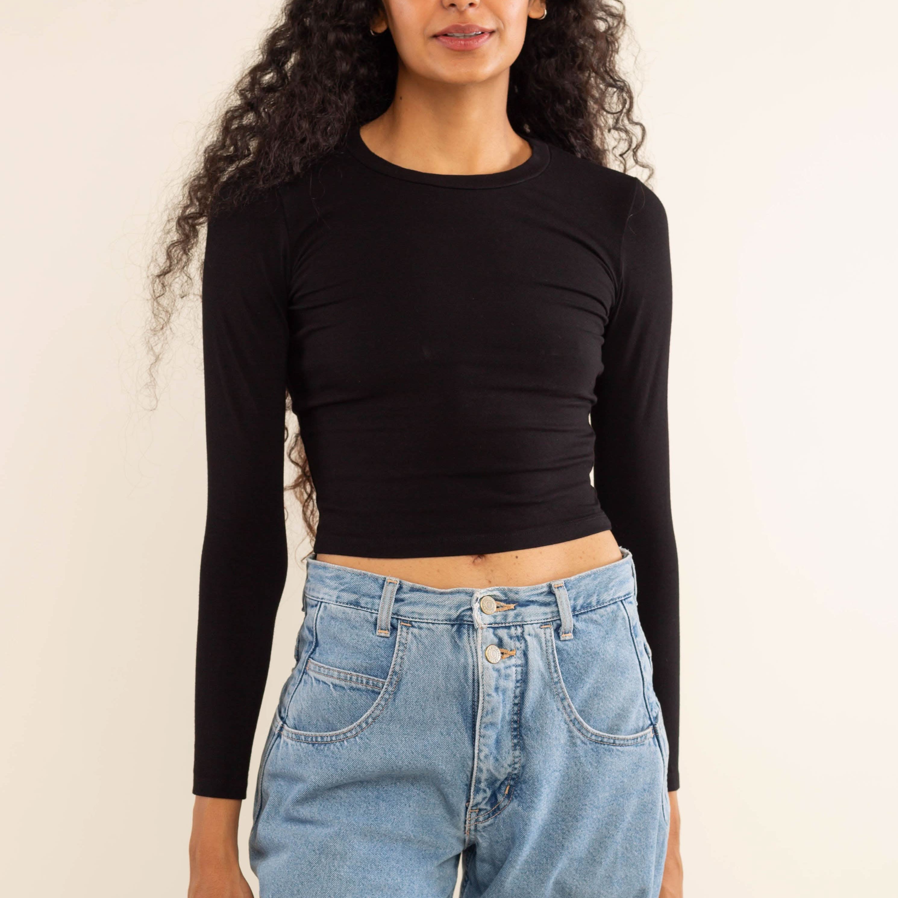 Woman wearing white, long sleeve, tight, crew neck, top with blue jeans