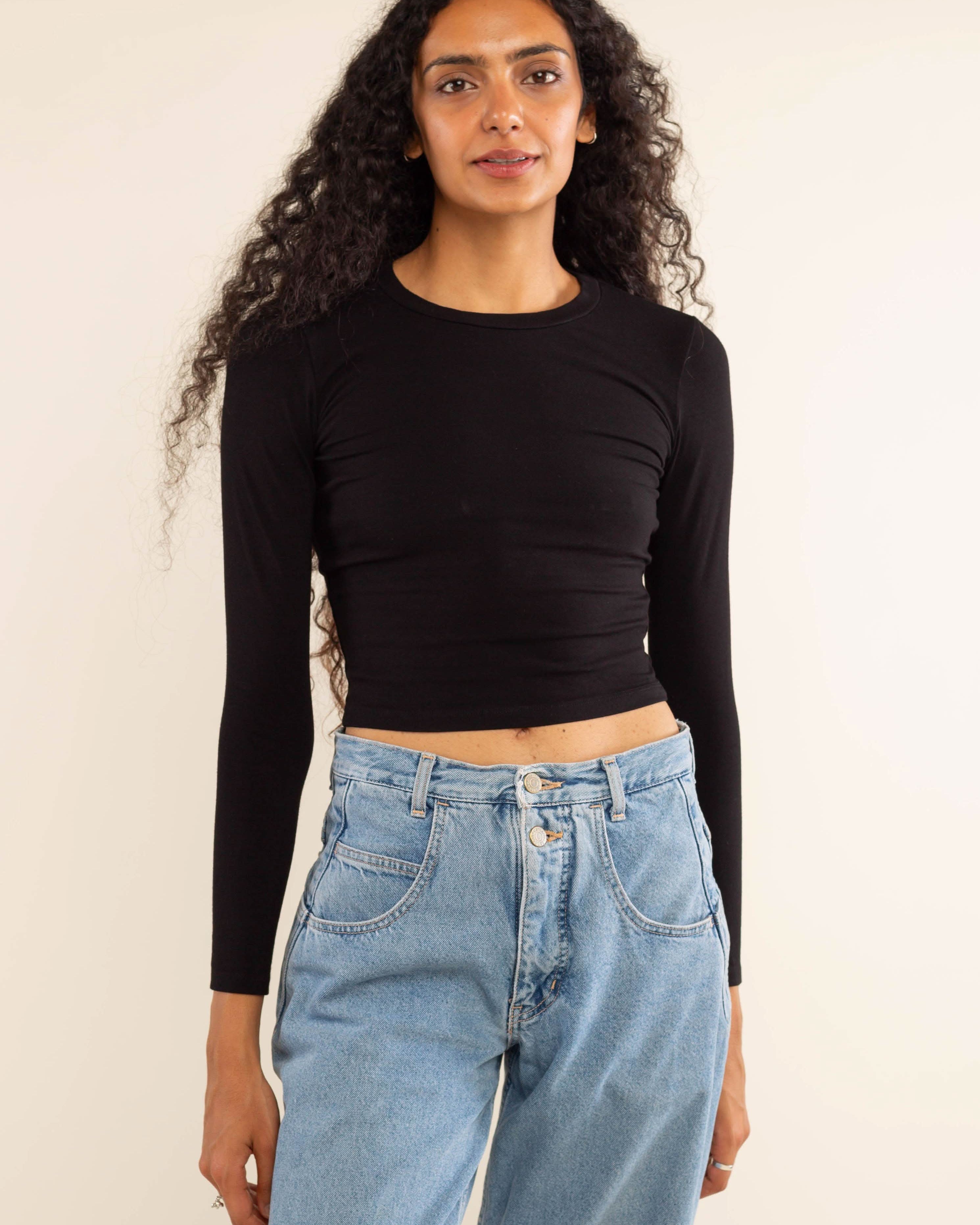 Woman wearing white, long sleeve, tight, crew neck, top with blue jeans
