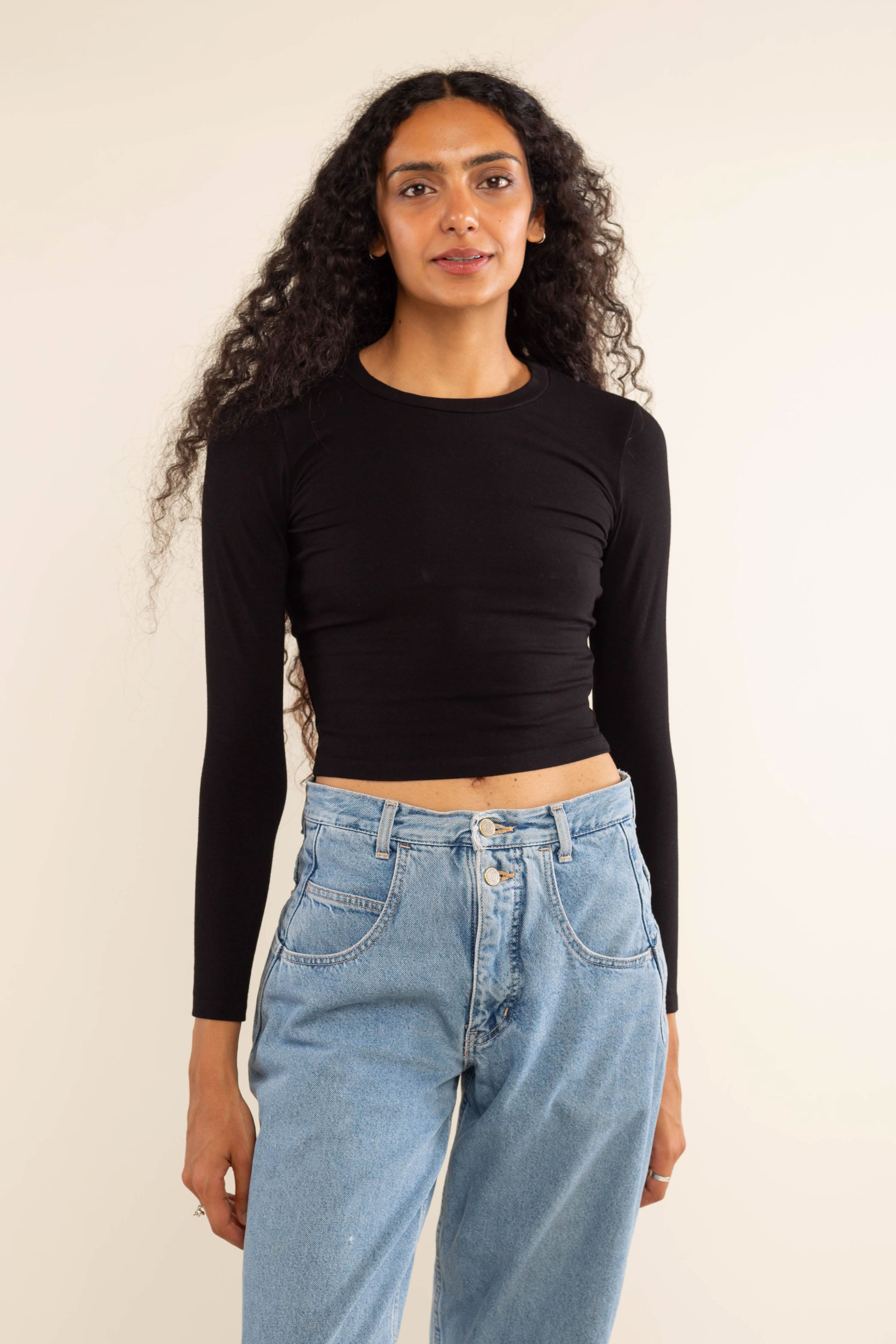Woman wearing white, long sleeve, tight, crew neck, top with blue jeans