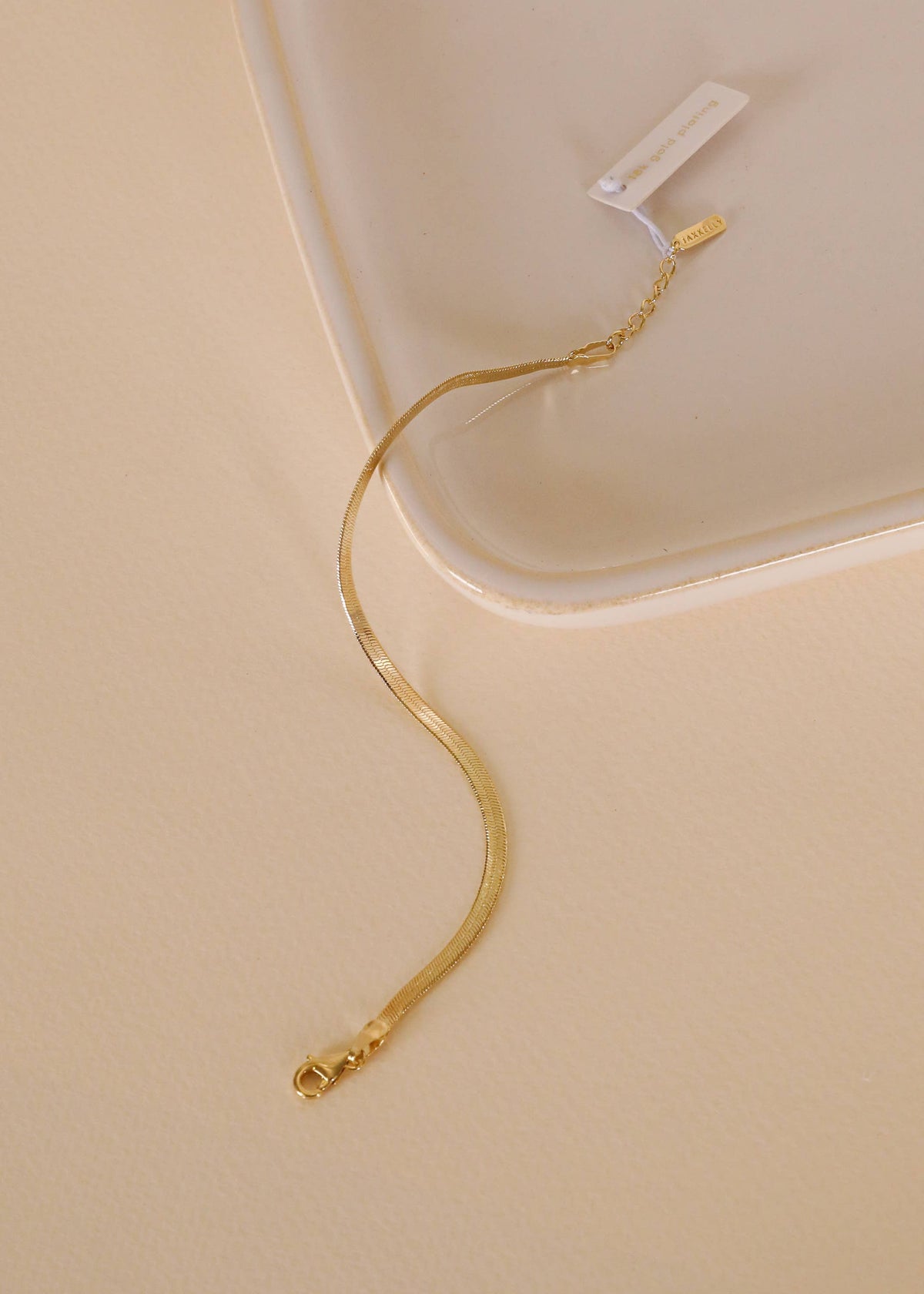 Gold bracelet on a beige surface with a white background