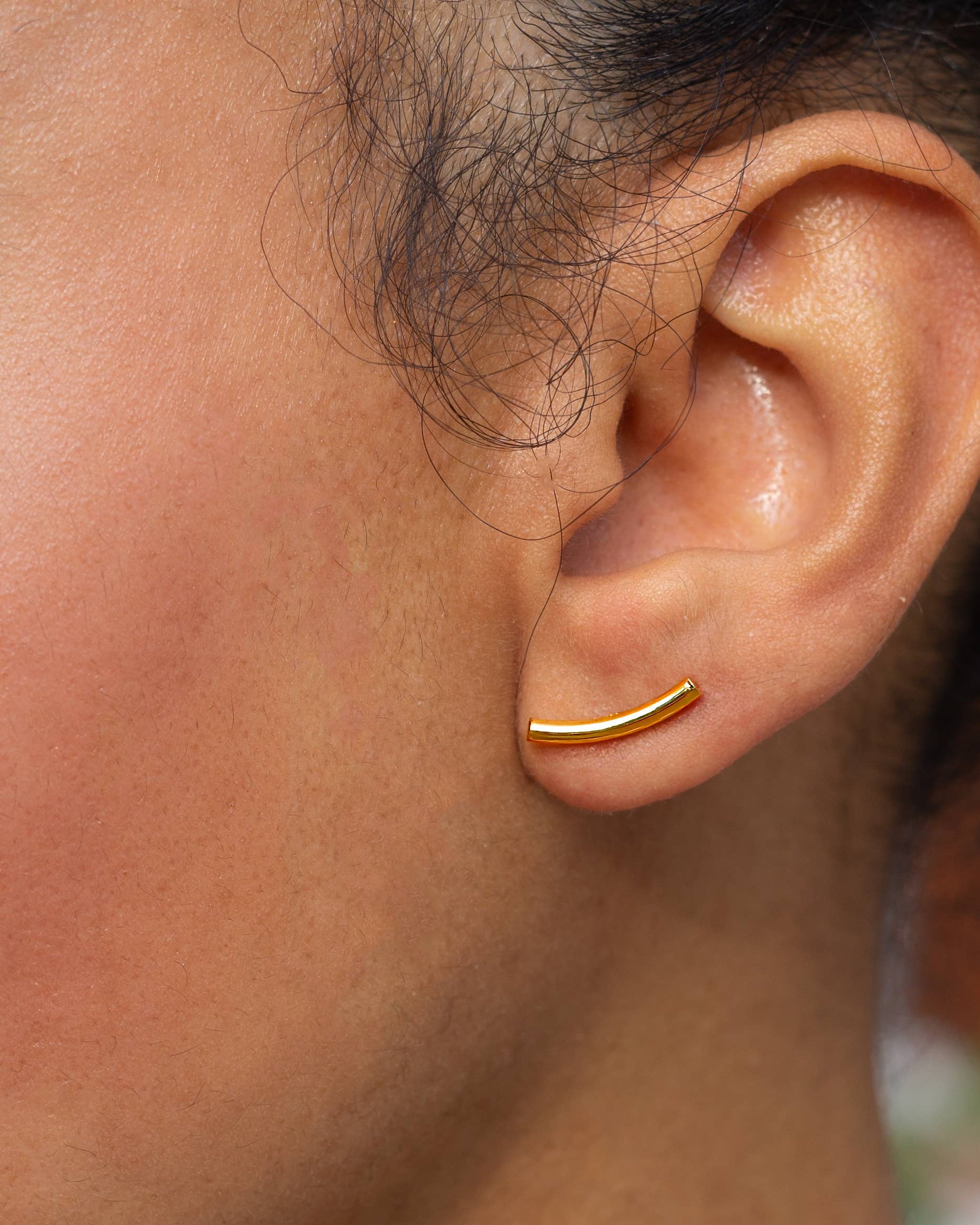 Close-up of an ear wearing a gold hoop earring with blurred background