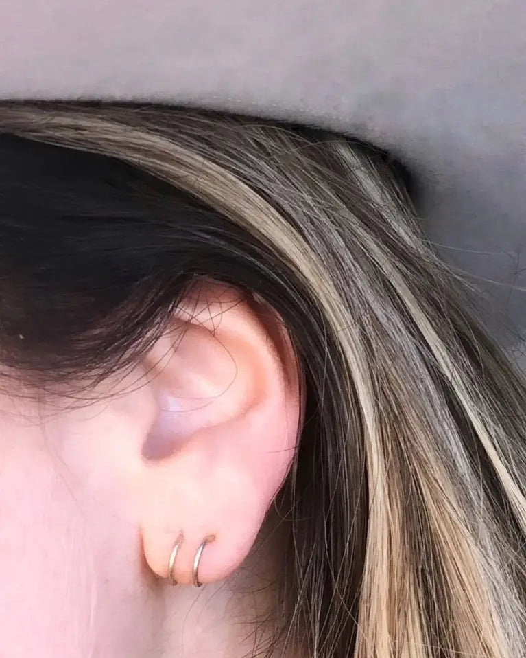 Close-up of an ear with a gold hoop earring against a neutral background