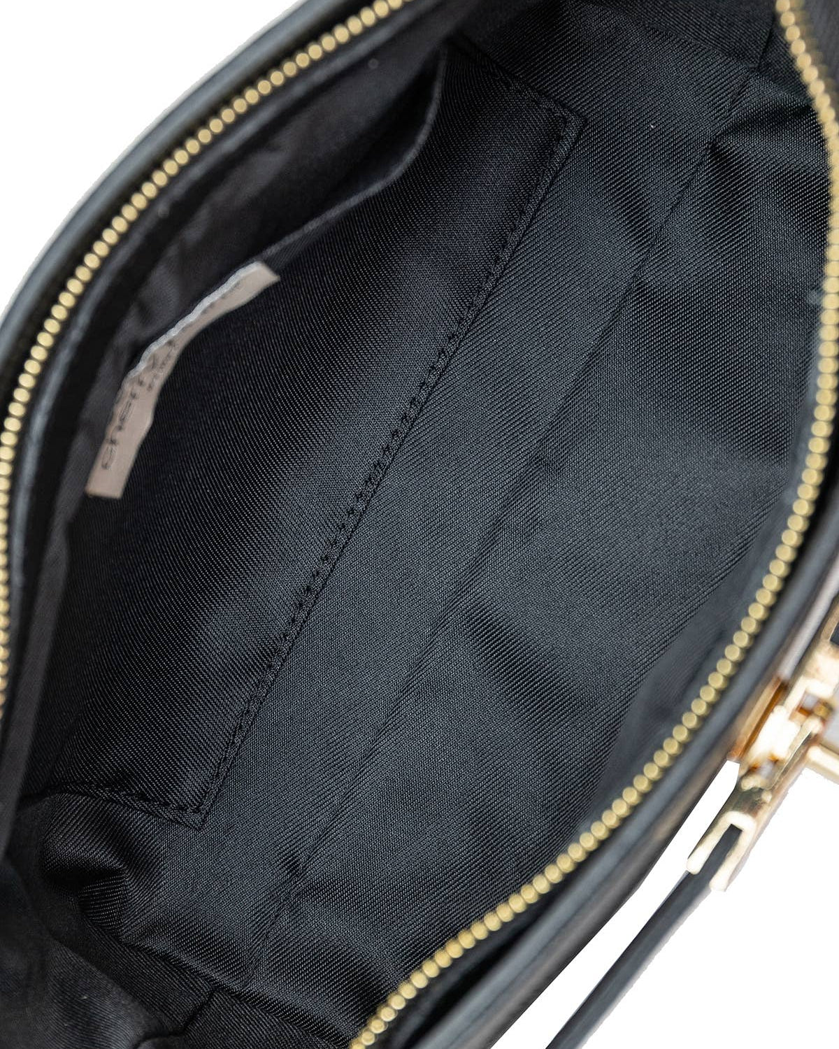 Close-up of the interior of a black handbag or clutch, showing a black fabric lining, a zippered opening with gold-tone zipper teeth, and part of the exterior material at the top right.