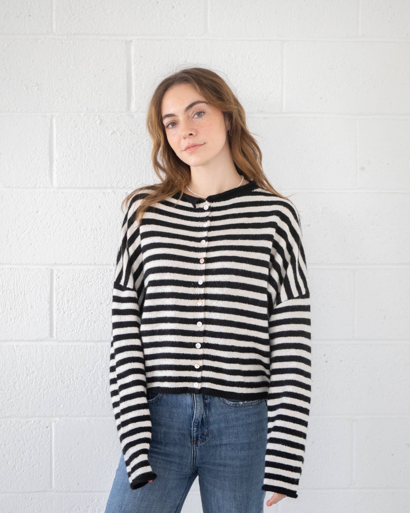 Woman wearing a black and white striped shirt against a white brick wall