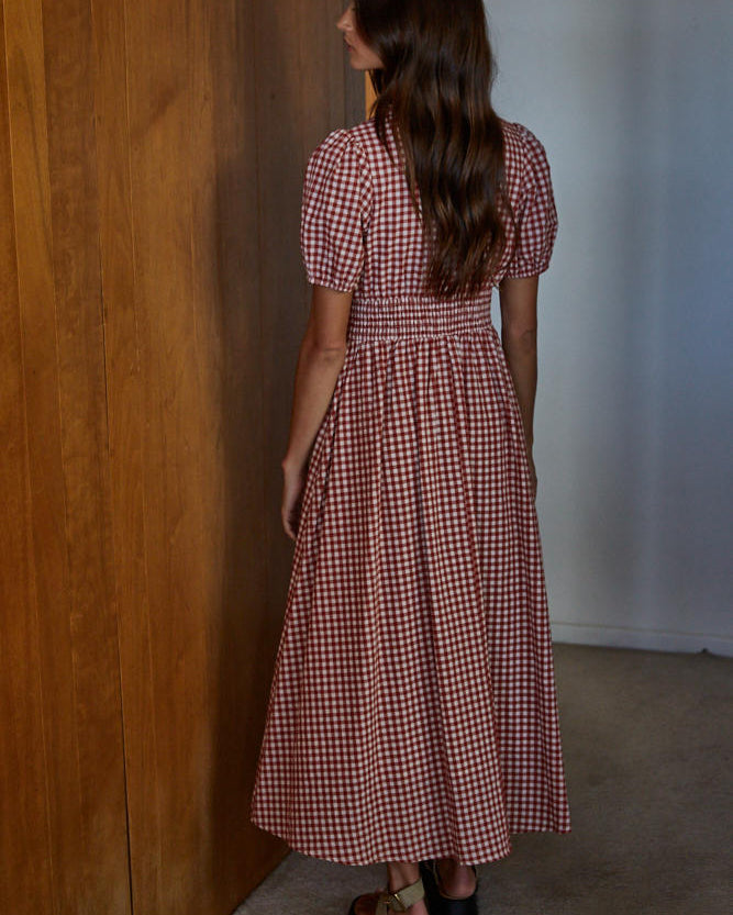 Woman in a red and white checkered dress standing in a room with wooden walls.