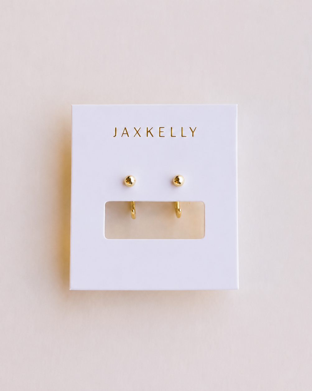 Gold earrings on a Jaxkelly branded card against a beige background