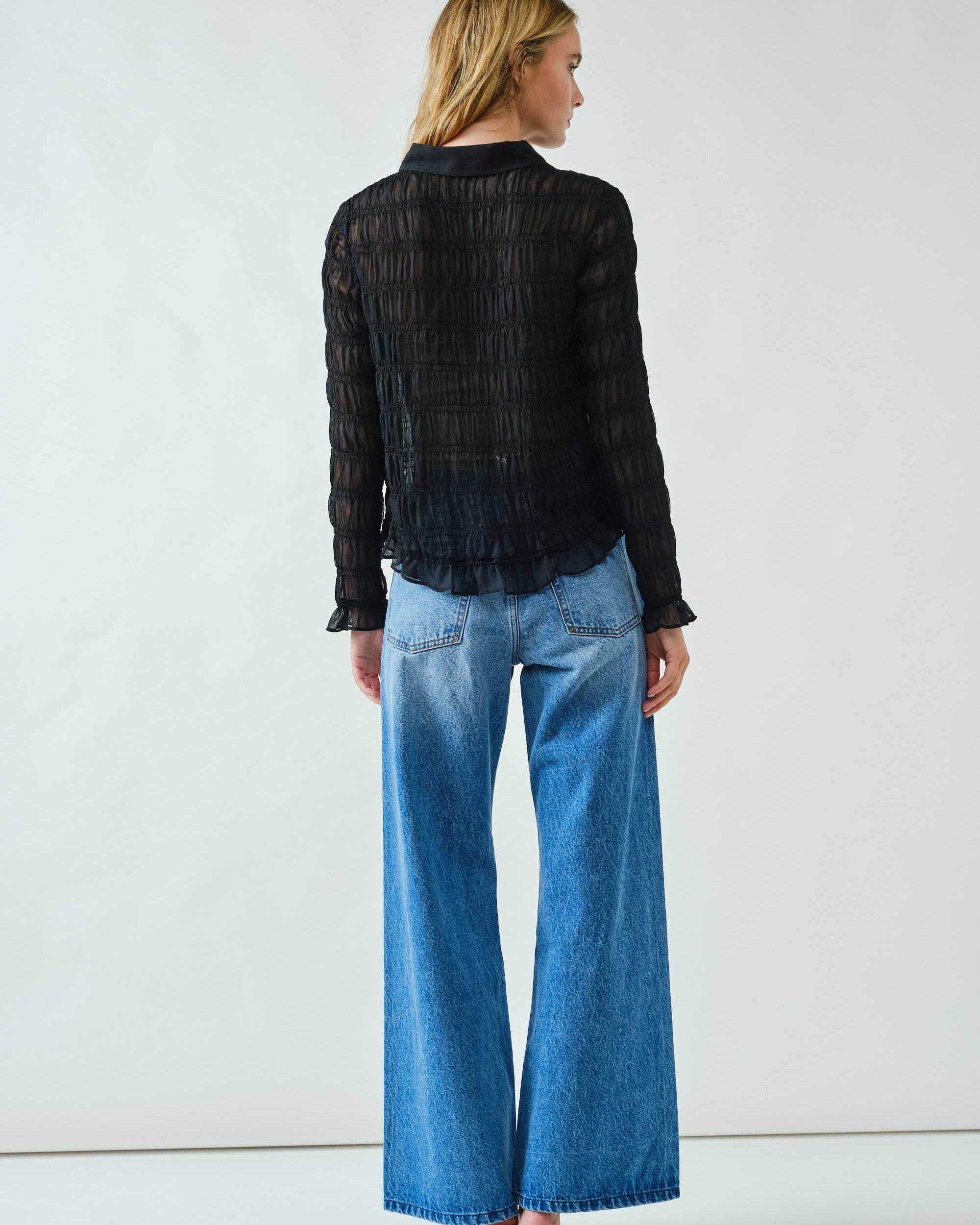 Woman wearing a black striped shirt and blue jeans against a white background