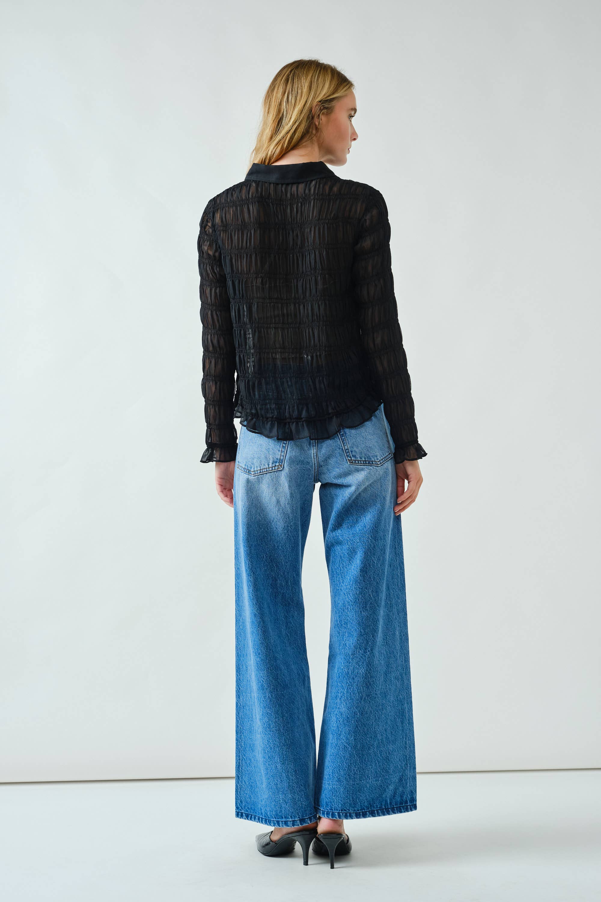 Woman wearing a black striped shirt and blue jeans against a white background