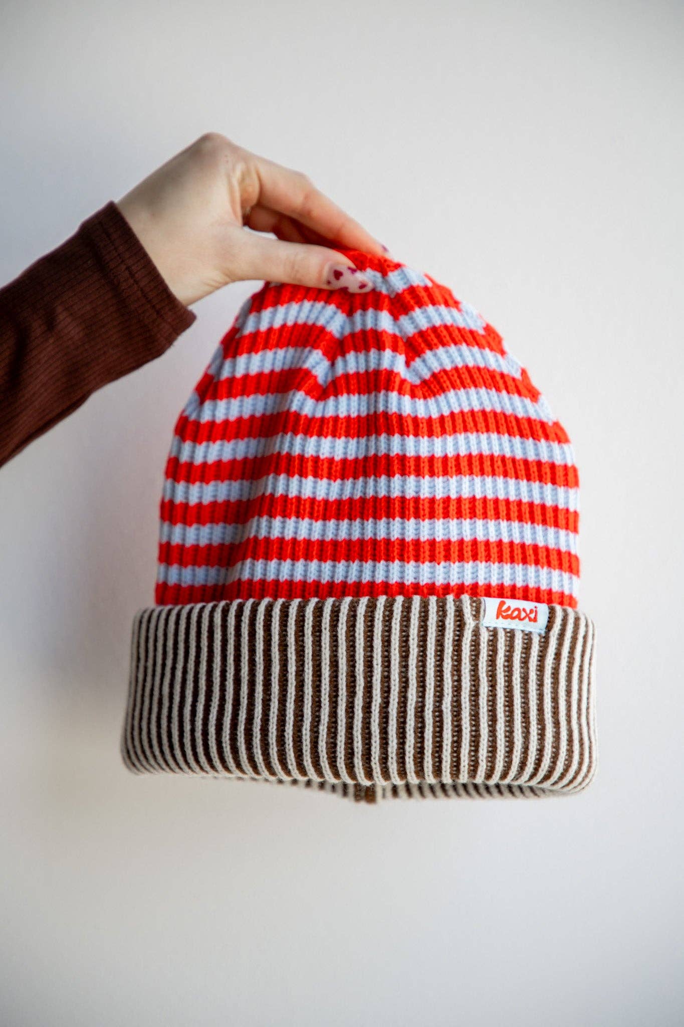 Striped beanie with red, white, and brown pattern held by a hand against a plain background