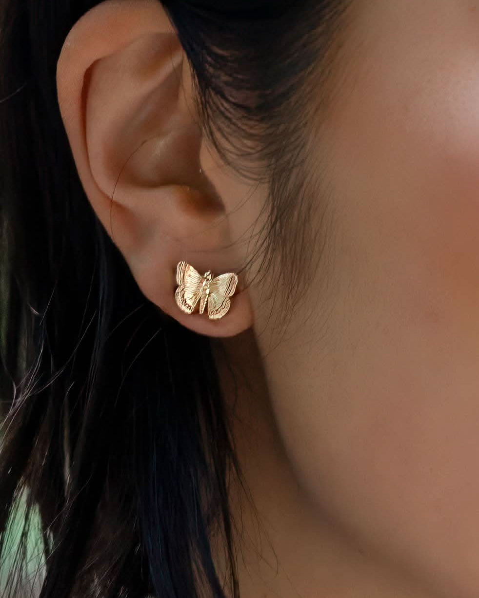 Woman wearing medium sized gold butterfly earrings with ridged wing details