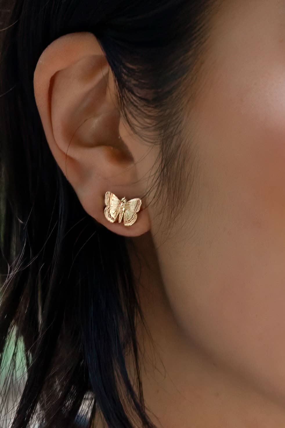 Woman wearing medium sized gold butterfly earrings with ridged wing details