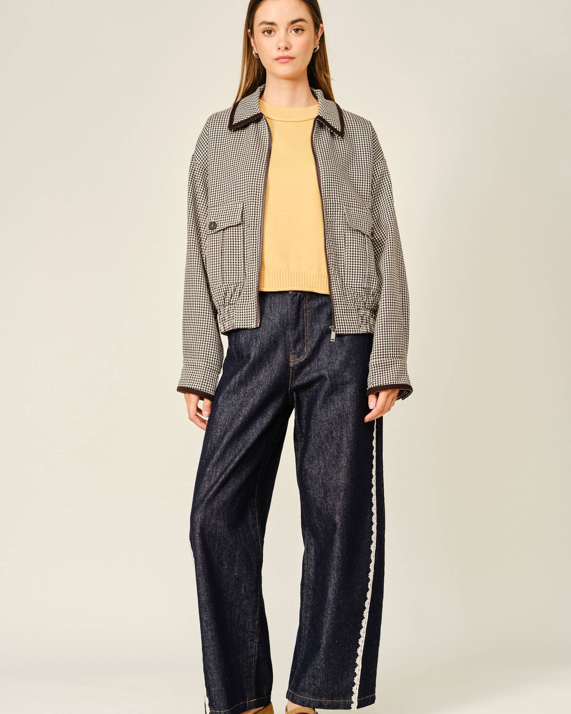 Woman wearing a checkered jacket, yellow top, and dark jeans on a plain background