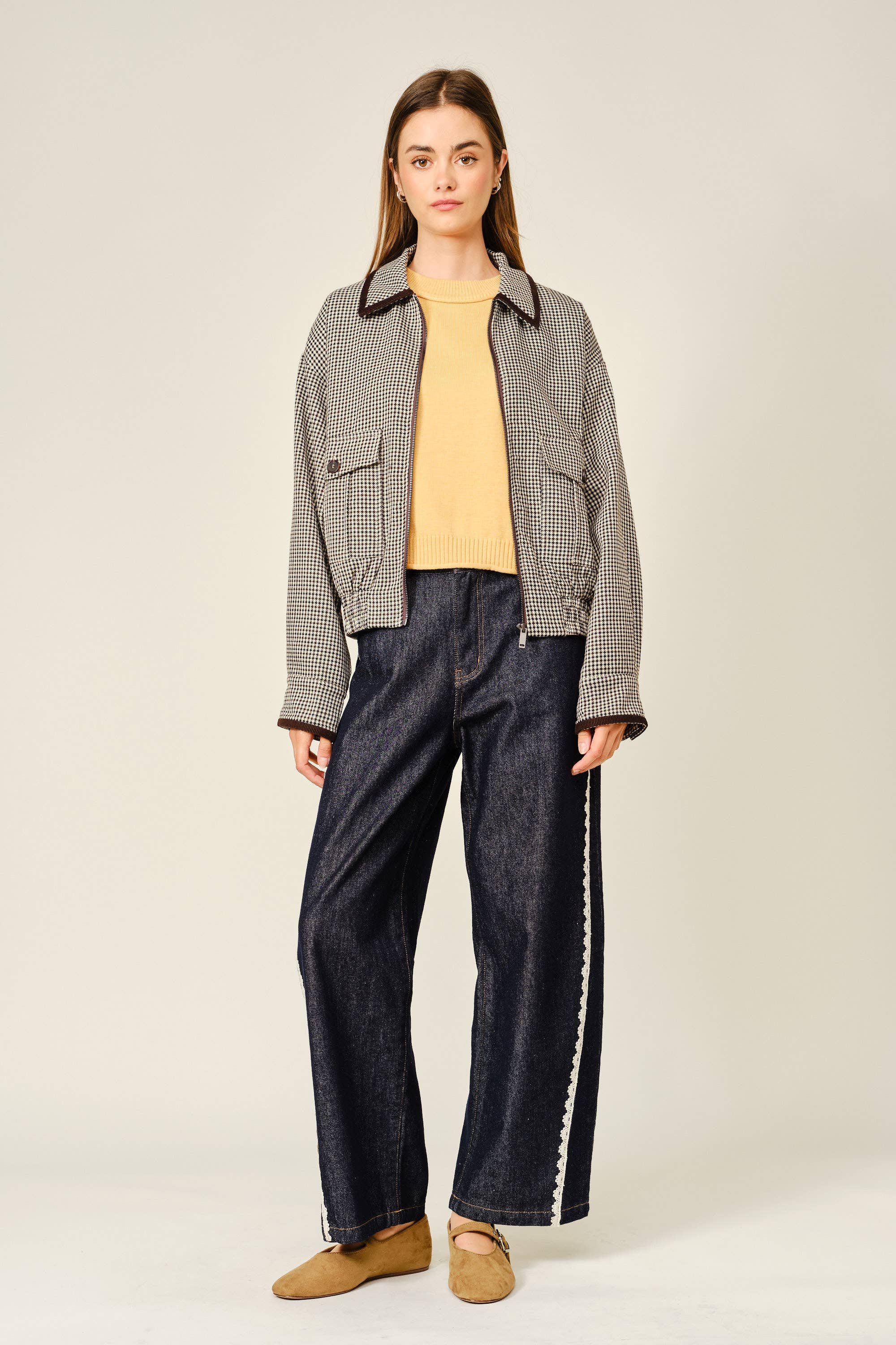 Woman wearing a checkered jacket, yellow top, and dark jeans on a plain background