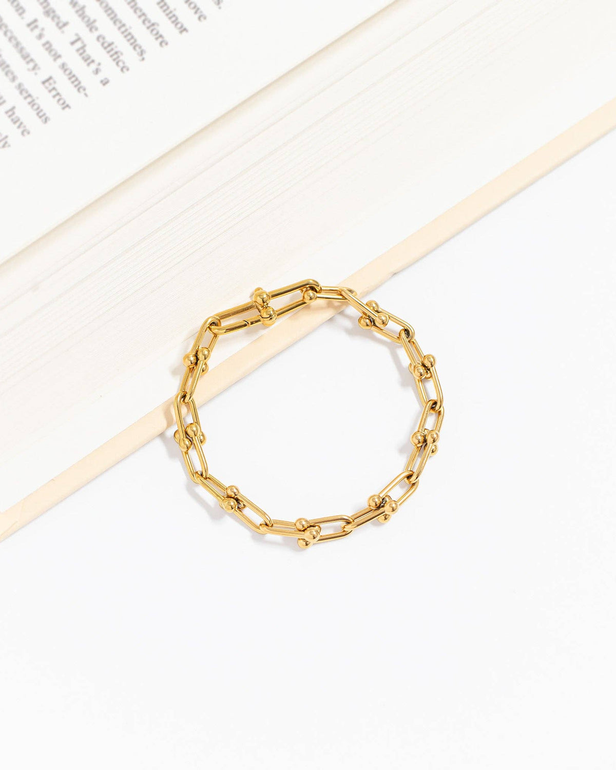 Gold chain bracelet on a white surface with a book in the background