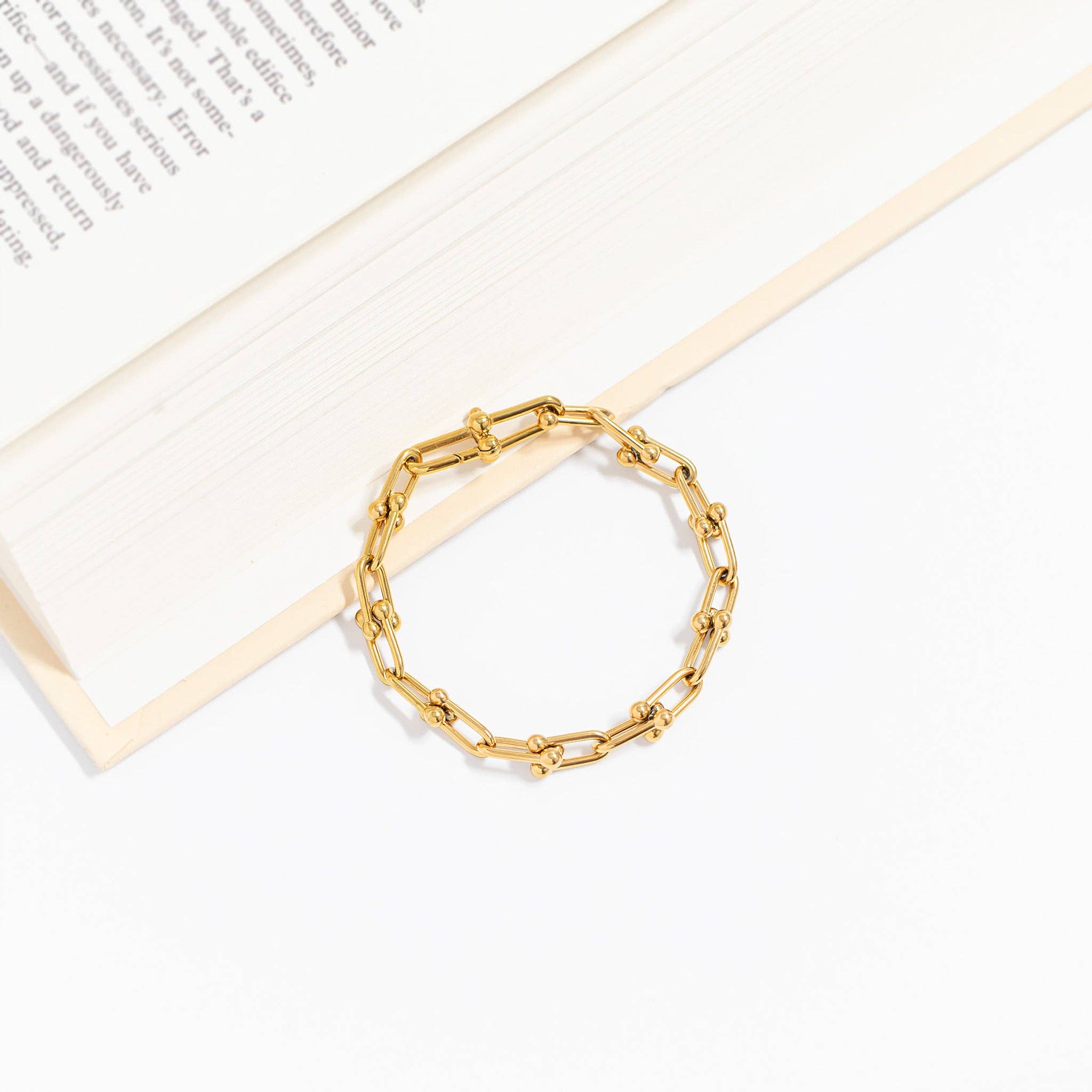 Gold chain bracelet on a white surface with a book in the background