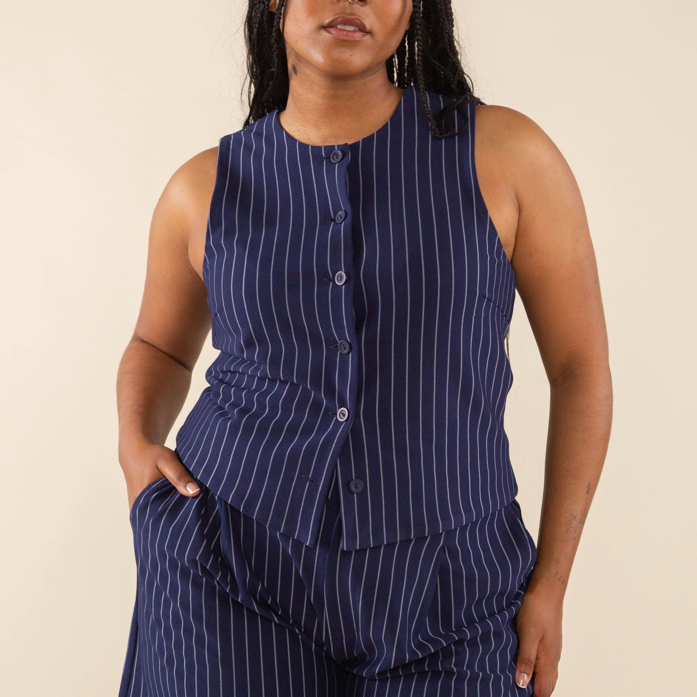 Woman wearing navy blue high neck vest with cream pinstripes. Vest has navy blue buttons all the way down