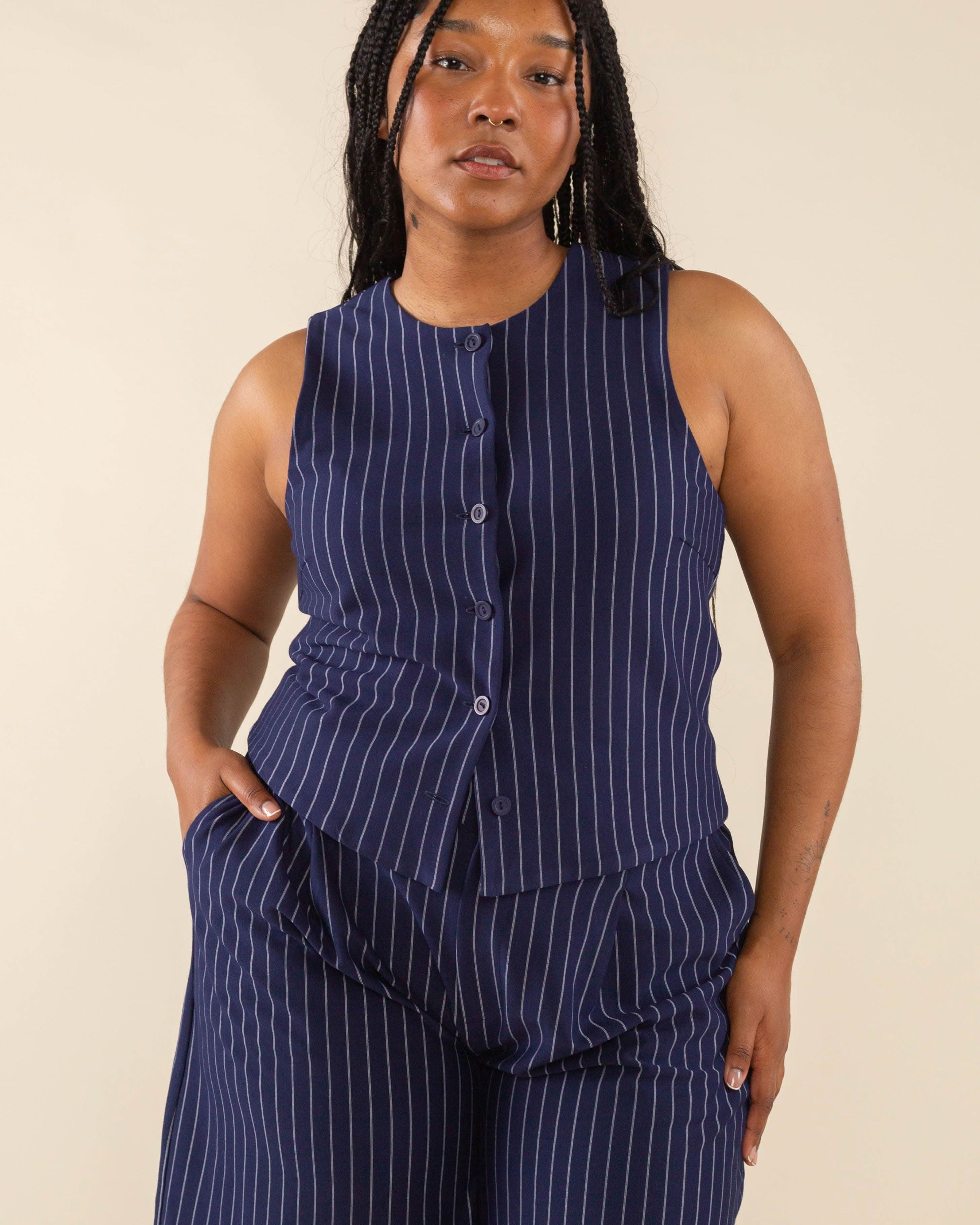 Woman wearing navy blue high neck vest with cream pinstripes. Vest has navy blue buttons all the way down