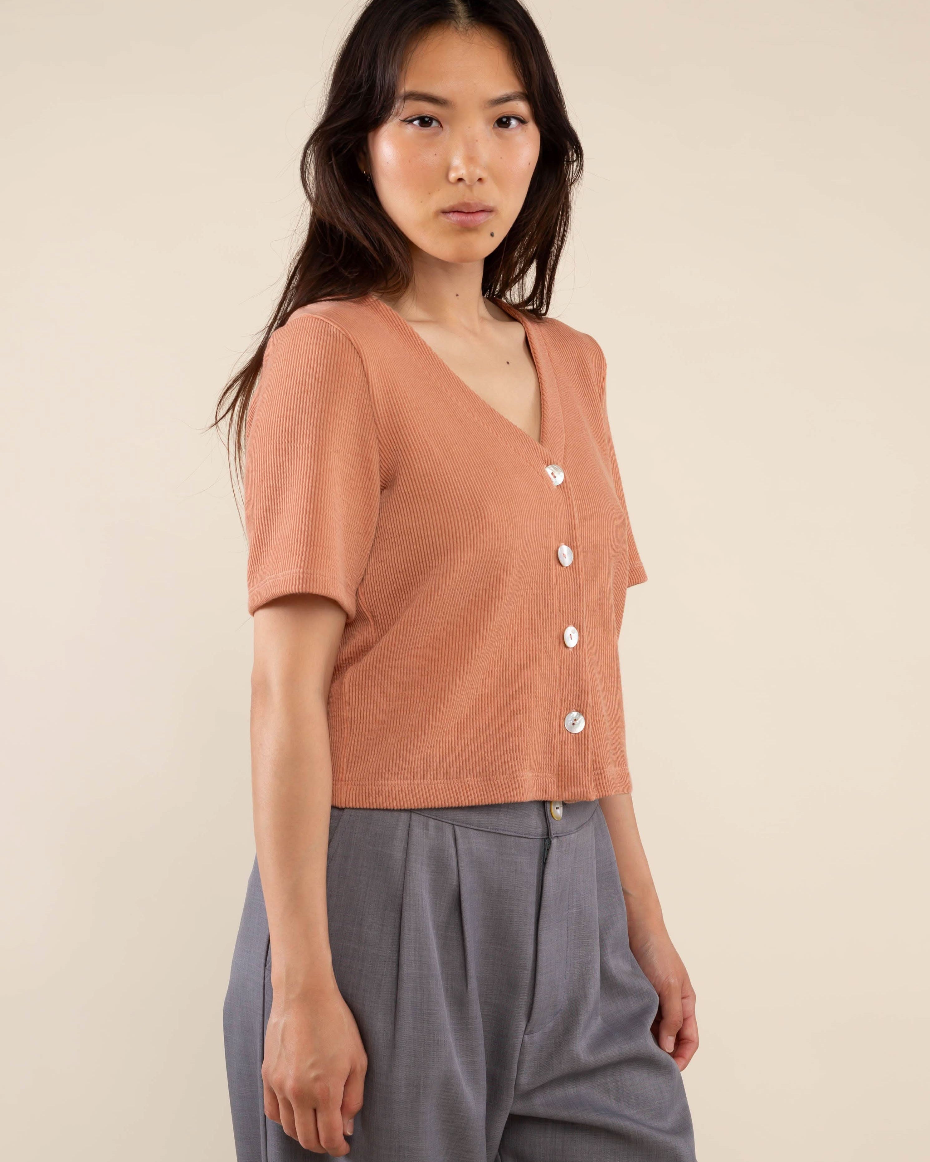 Woman wearing brick colored, ribbed, button down, short sleeve blouse top and grey pants