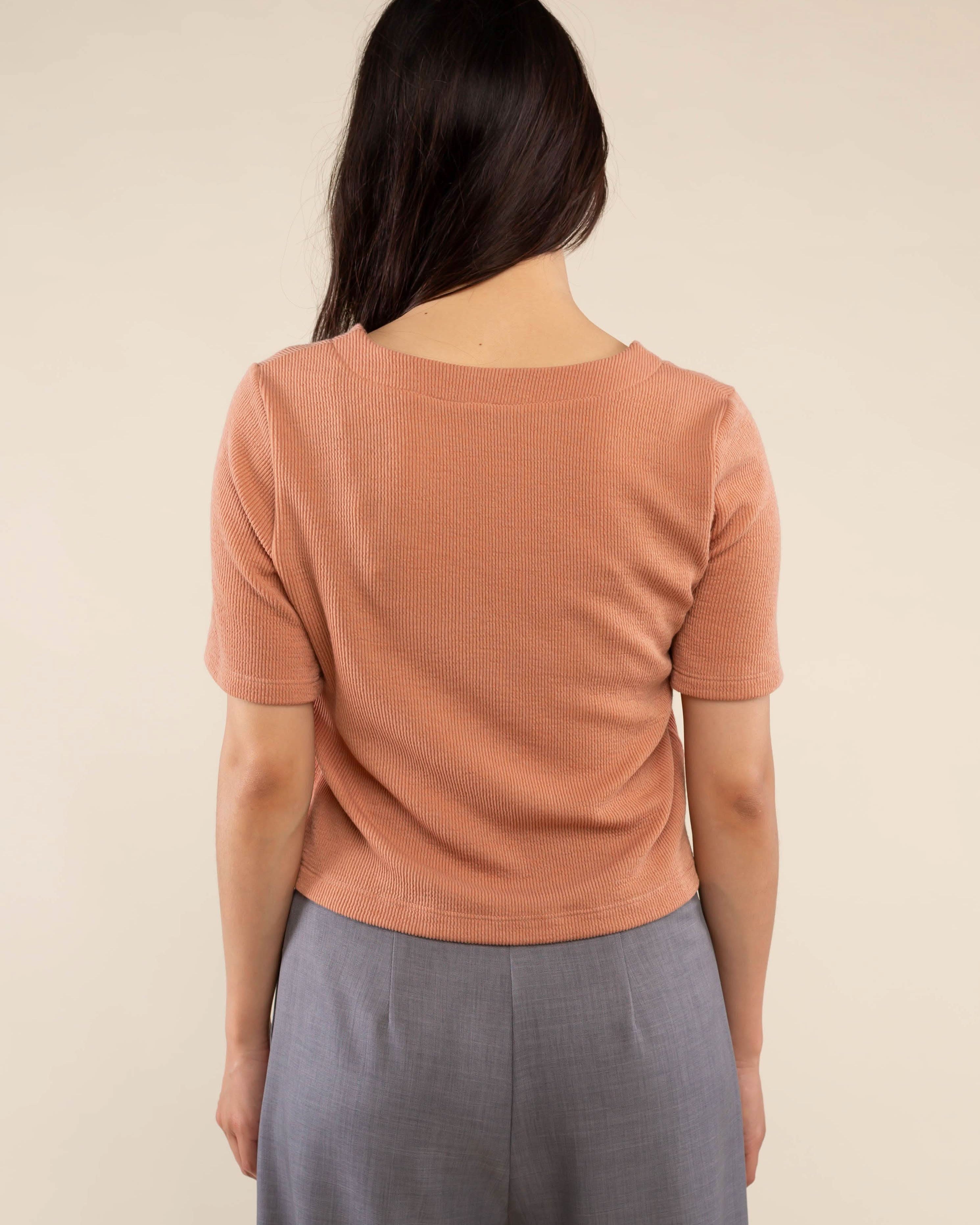 Woman wearing brick colored, ribbed, button down, short sleeve blouse top and grey pants