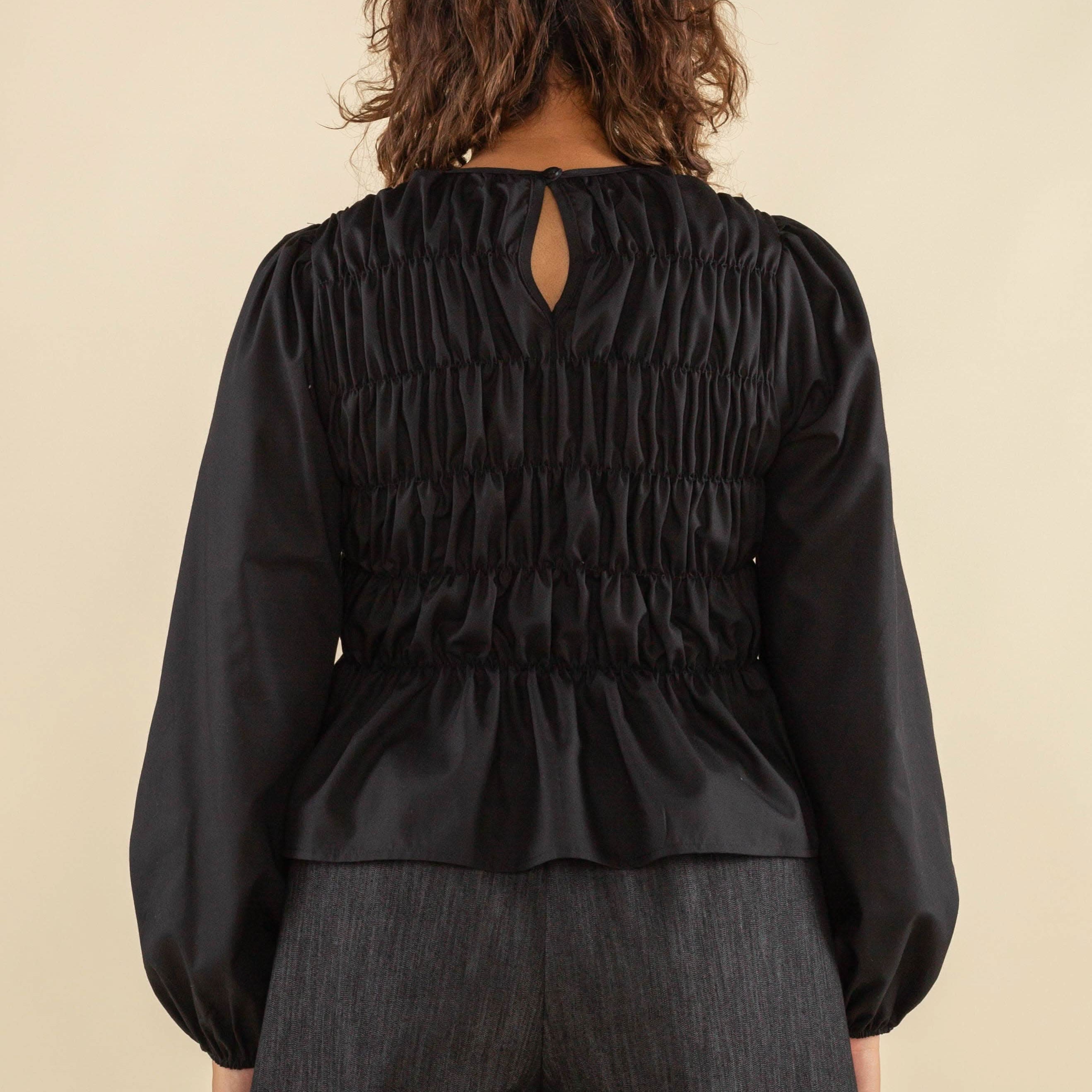 Woman facing away from the camera wearing black, bubble long sleeve, shirred, peplum style top with back eye detail