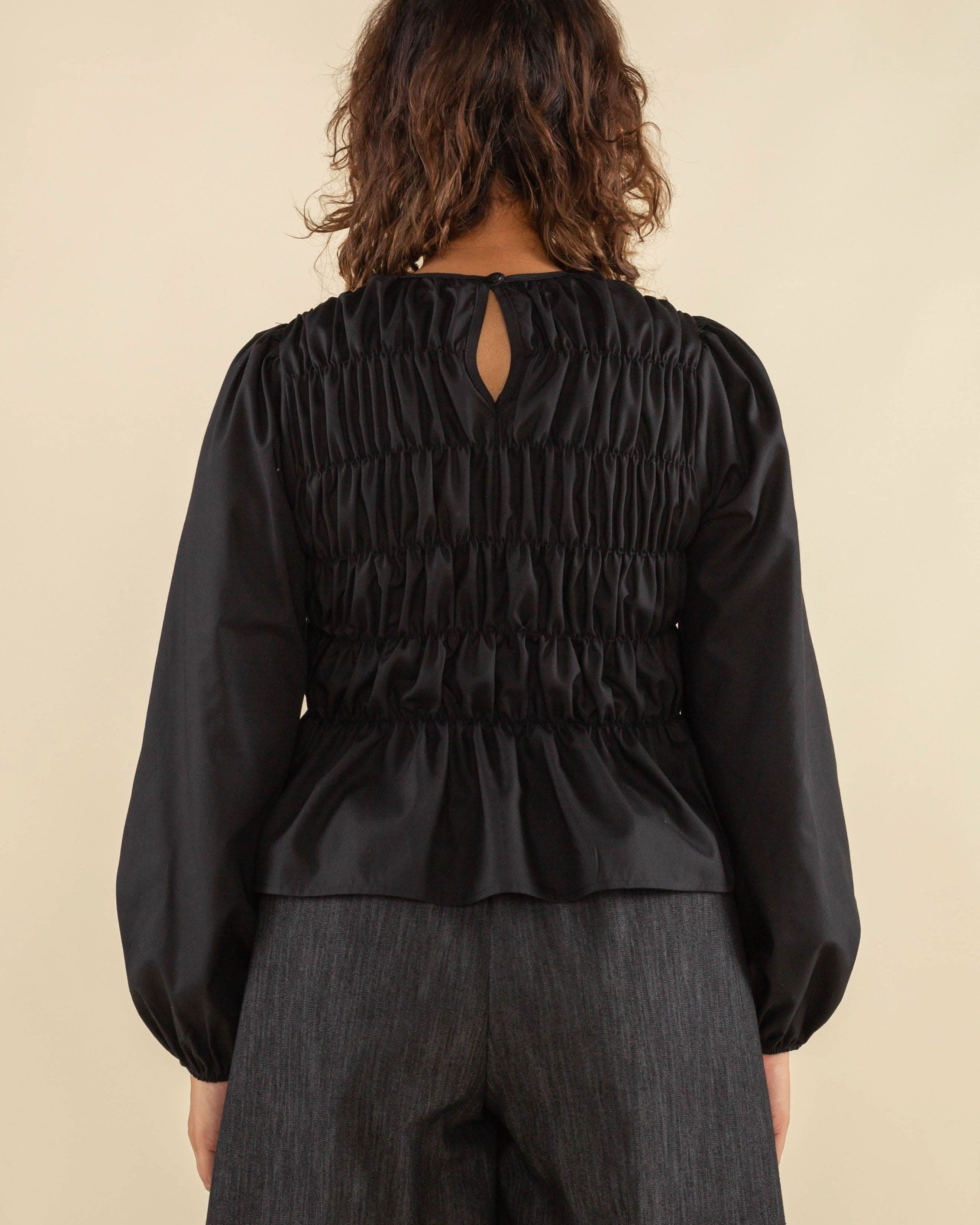 Woman facing away from the camera wearing black, bubble long sleeve, shirred, peplum style top with back eye detail