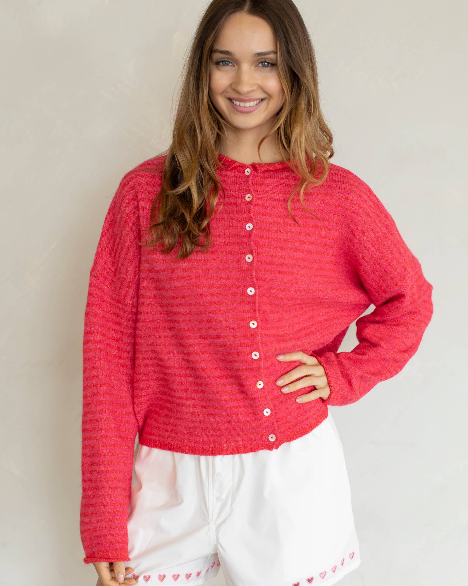 Woman wearing a red textured shirt and white shorts with heart patterns against a plain background