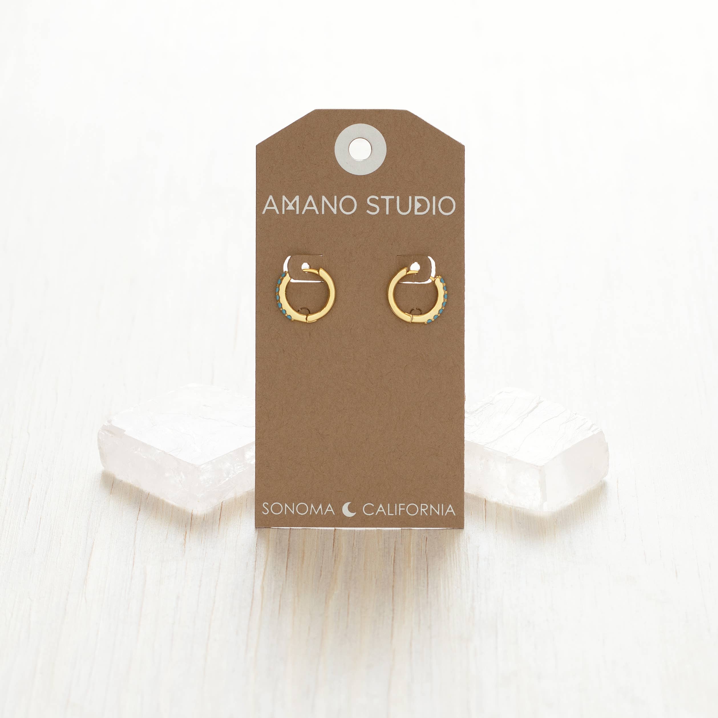 Gold hoop earrings on a brown Amano Studio card with a white background