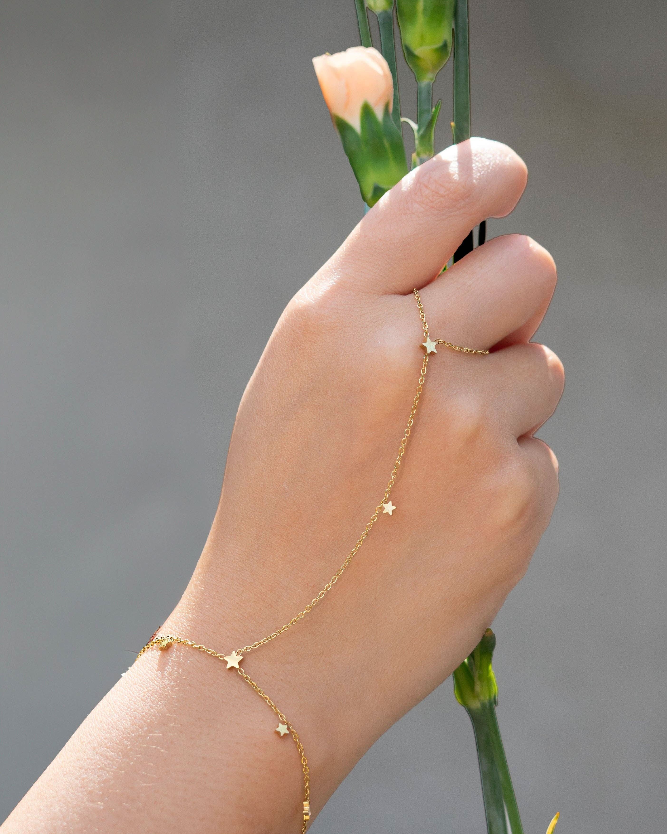 Hand wearing a delicate gold hand chain bracelet connected to a thin ring