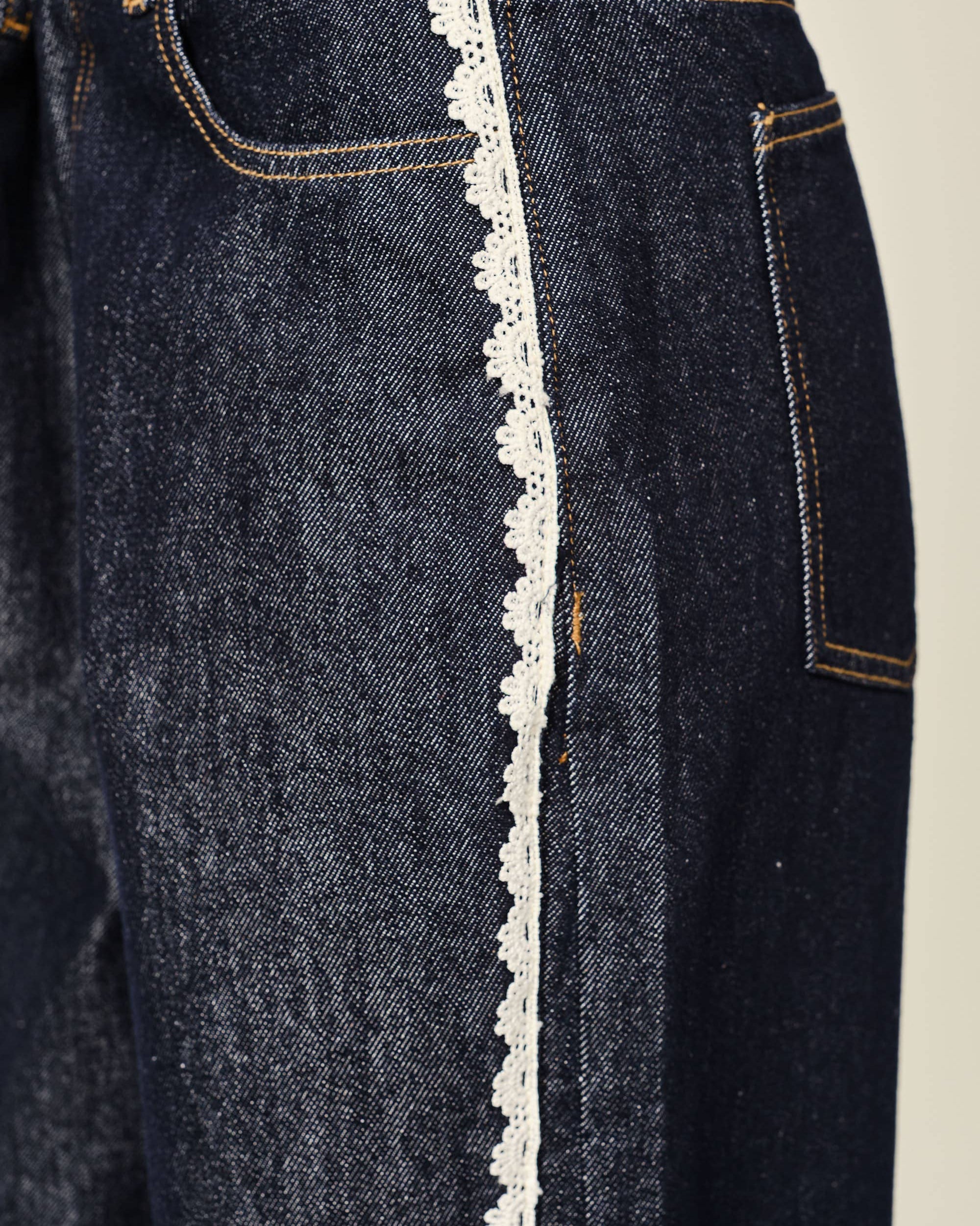 Dark blue jeans with white lace trim on a beige background