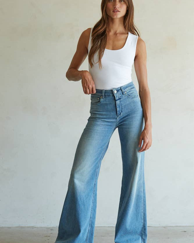 Woman wearing a white tank top and blue jeans against a plain background