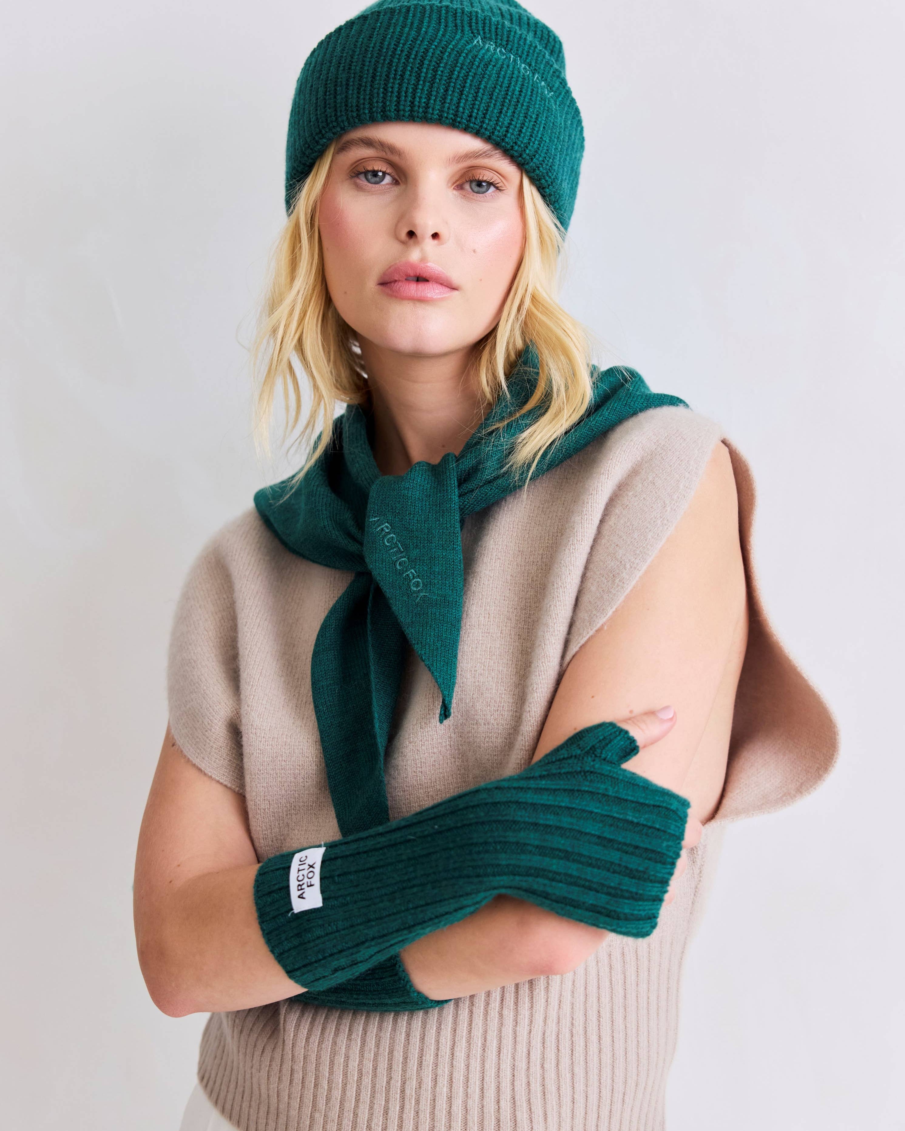 Woman wearing a green knit hat, scarf, and gloves against a white background