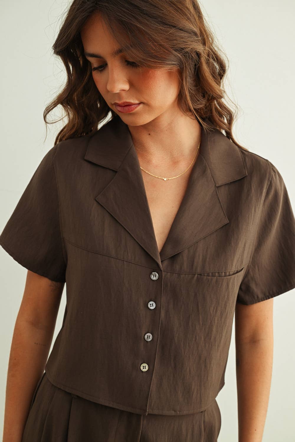 Woman wearing a brown short-sleeve blouse with a plain background