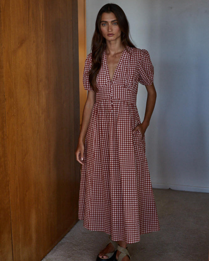 Woman wearing a red and white checkered dress standing against a wooden wall.