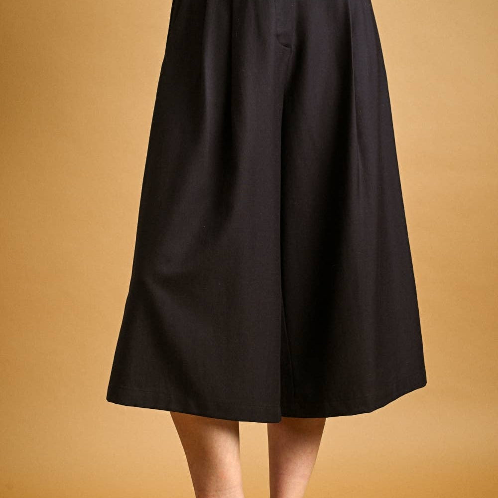 A person wearing a black wide-leg midi skirt, styled with a black and white striped top and brown leather loafers, against a solid warm tan background.