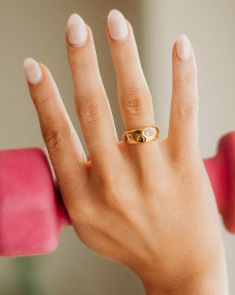 Gold ring with multi shaped and colored gems across the thickest head of the ring