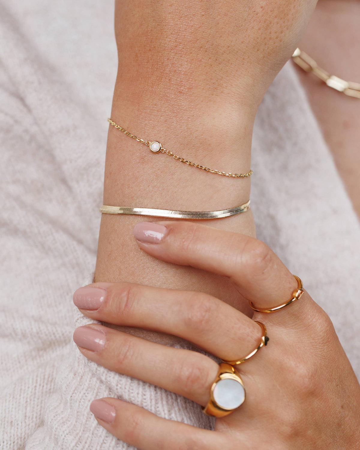 Close-up of a hand wearing gold bracelets and rings on a neutral background