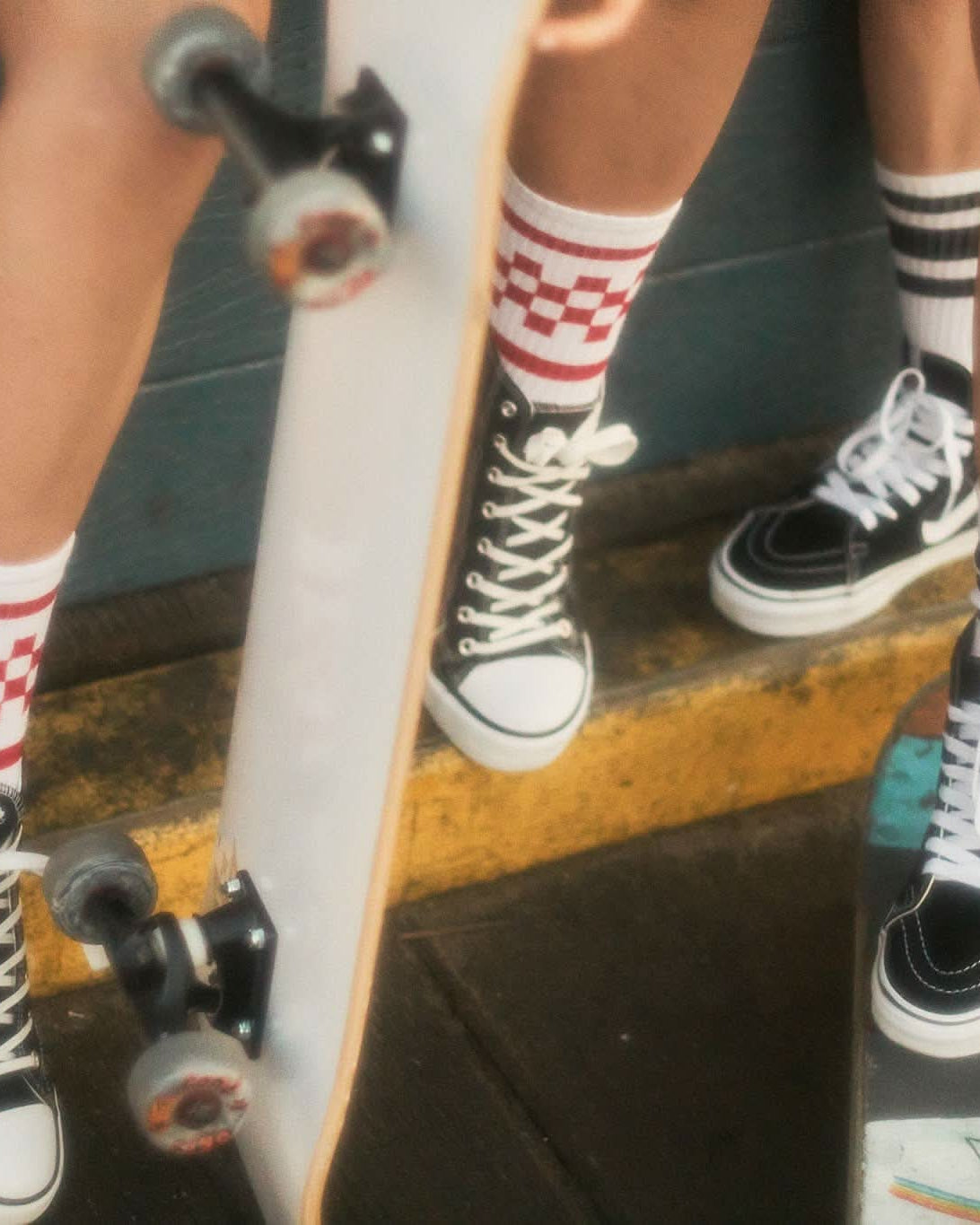 Person wearing checkered socks and black sneakers with a skateboard on a concrete surface.
