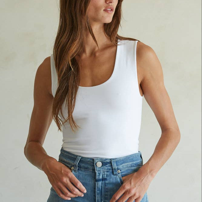 Woman wearing a white tank top and blue jeans against a plain background